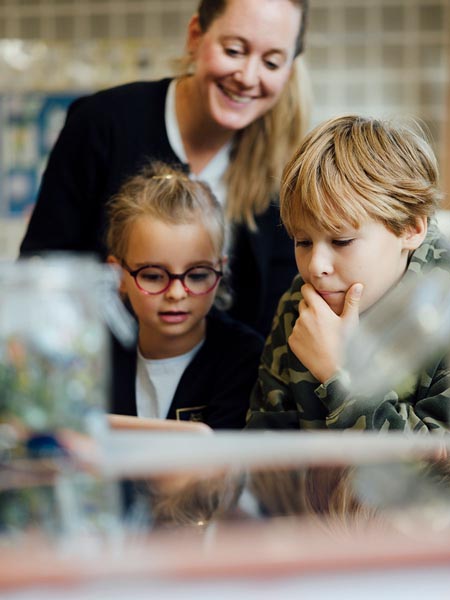 Eine Lehrerin, eine Grundschülerin und ein Grundschüler blicken gemeinsam in einen Tabletcomputer